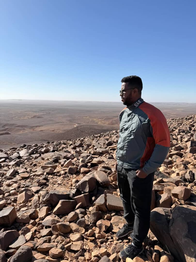 Nomadic guardian in traditional Mauritanian attire standing in the vast Sahara desert landscape